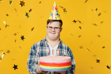 Young smiling man with down syndrome wear glasses casual clothes look camera hold birthday cake in...