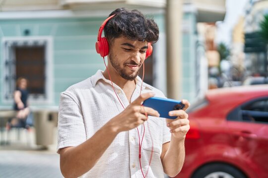 Young arab man smiling confident playing video game at street