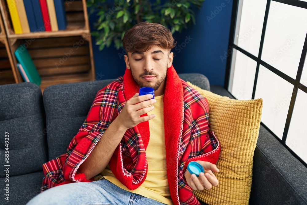 Poster young arab man smelling mint medication sitting on sofa at home