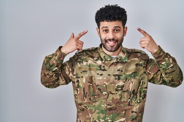 Arab man wearing camouflage army uniform smiling pointing to head with both hands finger, great idea or thought, good memory