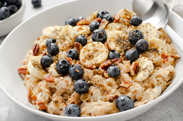 Oatmeal Bowl, Oat Porridge with Blueberry, Banana and Pecans in a Bowl on Bright Background, Healthy Snack or Breakfast