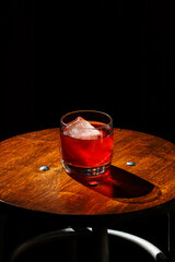 Closeup glass of negroni cocktail with ice at bar table isolated at black background.