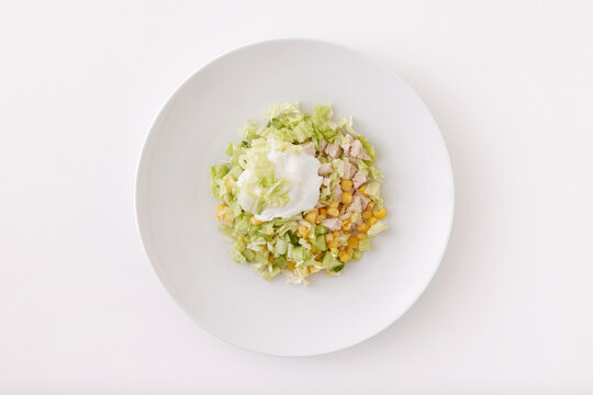 Plate of vegetable salad with cucumbers, corn and chicken isolated at white background.