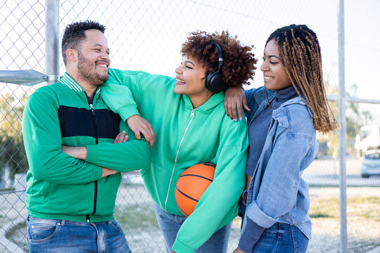A group of happy and diverse multi-ethnic friends gather together on a basketball court. The 3 friends talk and laugh while leaning on his shoulders. Concept of diversity in African groups.