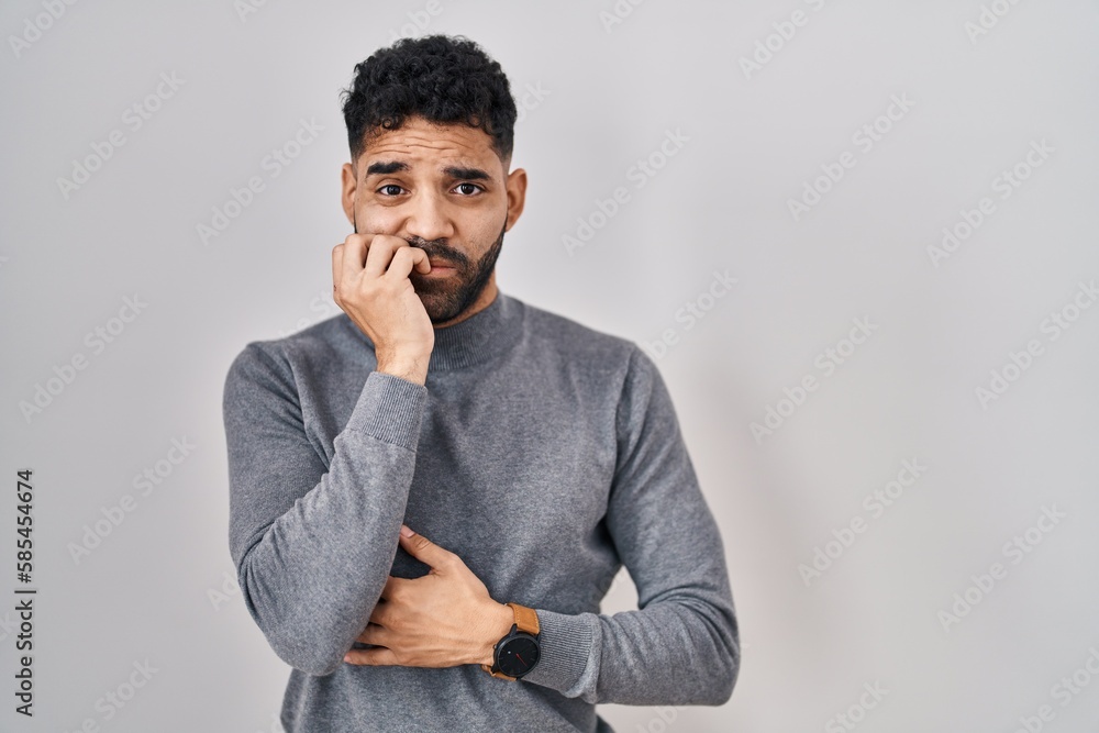 Canvas Prints Hispanic man with beard standing over white background looking stressed and nervous with hands on mouth biting nails. anxiety problem.