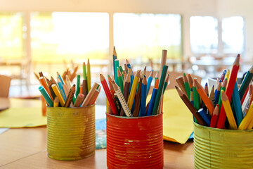 Farbige Konservendosen voller Buntstifte stehen auf einem Tisch im Schulzimmer