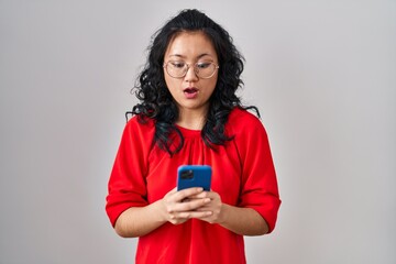 Young asian woman using smartphone typing message afraid and shocked with surprise and amazed expression, fear and excited face.