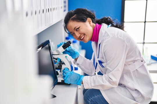 Young chinese woman scientist smiling confident using microscope at laboratory