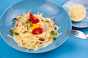Pasta with cheese and egg, bacon and tomatoes, microgreens. Food in a blue plate. Homemade carbonara pasta. Lunch on the table top view. Italian spaghetti with ham, cream