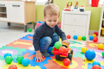 Adorable blond toddler playing with tractor and balls sitting on floor at kindergarten