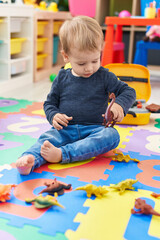 Adorable blond toddler playing with dino toys sitting on floor at kindergarten