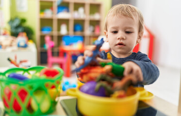 Adorable blond toddler playing with play kitchen standing at kindergarten
