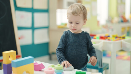Adorable blond toddler playing with geometry blocks standing at kindergarten