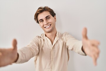 Young man standing over isolated background looking at the camera smiling with open arms for hug. cheerful expression embracing happiness.