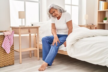 Middle age woman suffering for knee pain sitting on bed at bedroom