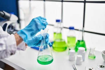 Fototapeta premium Young beautiful hispanic woman scientist pouring liquid on test tube at laboratory