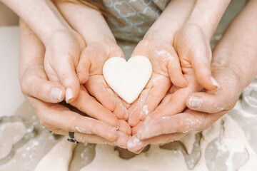 Grandmother's and mother's hands hold children's hands with heart-shaped dough. Happy childhood...