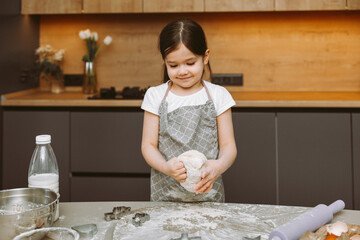 happy little girl making dough in the kitchen. a small child learns to cook food or bake yeast dough with his hands at home