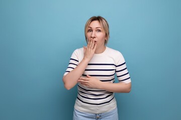 indignant blond girl in a striped sweater is surprised on a blue background with copy space