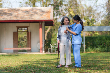 Fototapeta premium Asian nurse or female caregiver helping senior woman holding cane to walk in the hospital garden.