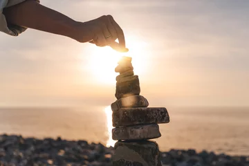 Cercles muraux Zen Woman building a stone pyramide on the seashore at sunset. Zen relaxation and meditation concept, close up shot