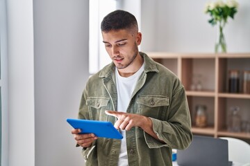Young hispanic man using touchpad standing at home