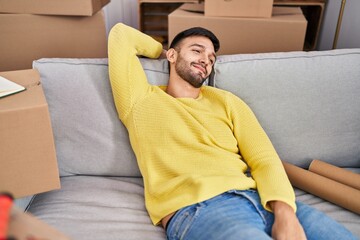Fototapeta premium Young hispanic man smiling confident relaxed on sofa at new home