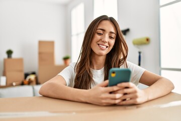 Young hispanic woman smiling confident using smartphone at new home