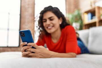 Young latin woman smiling confident using smartphone at home