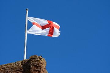 St George England flag fly's against a blue sky from the top of a historical building. Billowing  in the strong breeze. Copy space.