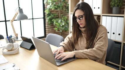 Beautiful hispanic woman business worker using laptop with serious face at office