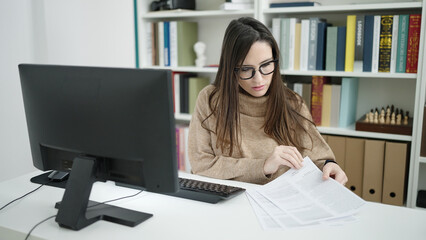 Beautiful hispanic woman student using computer reading document at library university