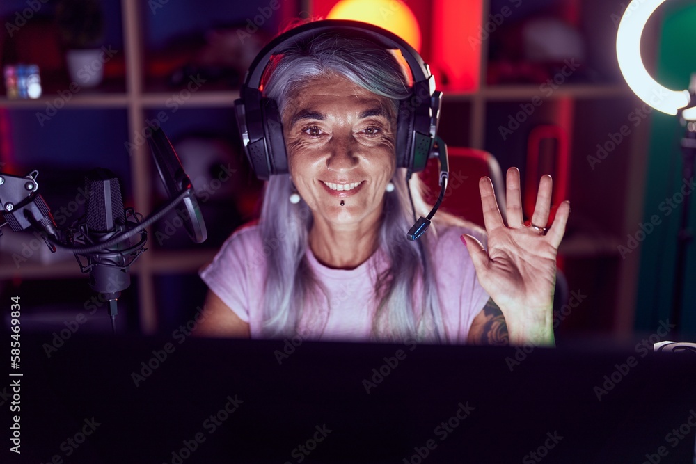 Sticker Middle age woman with tattoos playing video games wearing headphones looking positive and happy standing and smiling with a confident smile showing teeth