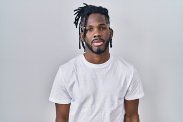 African man with dreadlocks wearing casual t shirt over white background relaxed with serious expression on face. simple and natural looking at the camera.