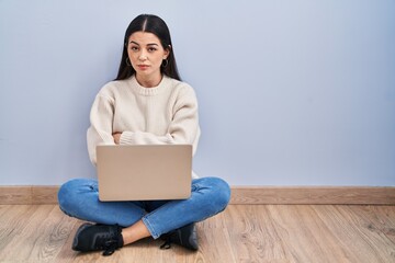 Young woman using laptop sitting on the floor at home skeptic and nervous, disapproving expression on face with crossed arms. negative person.