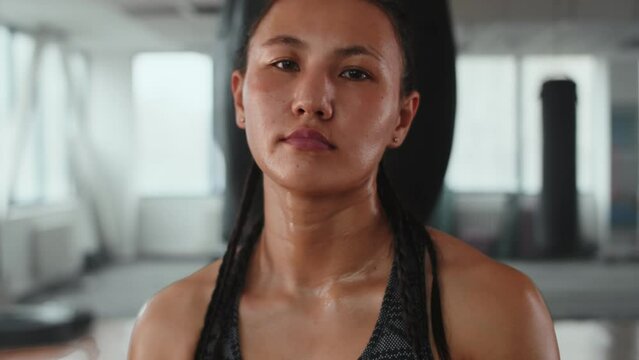 Portrait of a young asian female boxer with a confident face close up raising wrapped hands in starting position before training in an indoor boxing club