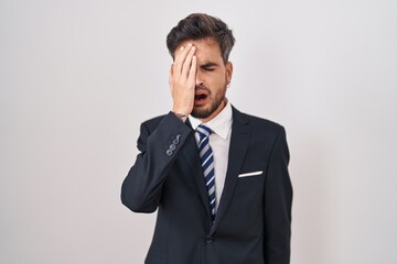 Young hispanic man with tattoos wearing business suit and tie yawning tired covering half face, eye and mouth with hand. face hurts in pain.