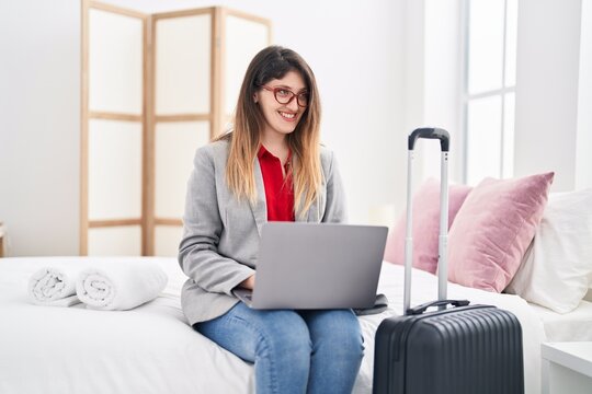 Young hispanic woman business worker using laptop sitting on bed at hotel room