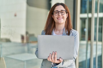 Young woman business worker smiling confident using laptop at street
