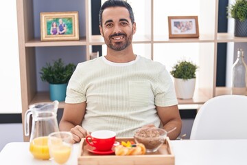 Fototapeta na wymiar Hispanic man with beard eating breakfast with a happy and cool smile on face. lucky person.