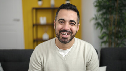 Fototapeta premium Young hispanic man smiling confident sitting on sofa at home