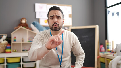 Young hispanic man teacher standing with no gesture at kindergarten