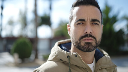 Young hispanic man standing with serious expression at park