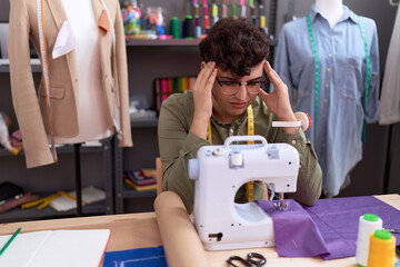 Non binary man tailor stressed using sewing machine suffering for headache at atelier