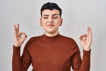 Non binary person wearing make up standing over isolated background relax and smiling with eyes closed doing meditation gesture with fingers. yoga concept.