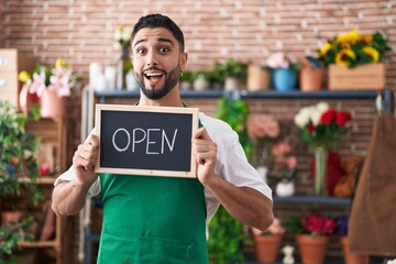 Hispanic young man working at florist holding open sign celebrating crazy and amazed for success with open eyes screaming excited.