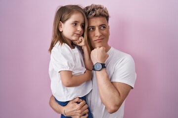 Young father hugging daughter over pink background serious face thinking about question with hand...