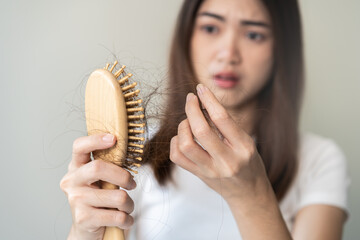 Serious asian young woman holding brush holding comb, hairbrush with fall black hair from scalp...