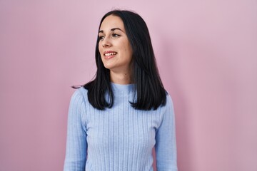 Fototapeta premium Hispanic woman standing over pink background looking away to side with smile on face, natural expression. laughing confident.