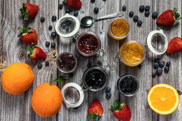 Assortment of homemade jams. Jams in glass jars, oranges, strawberries and blueberries. Top view of seasonal fruits in jam or marmalade.